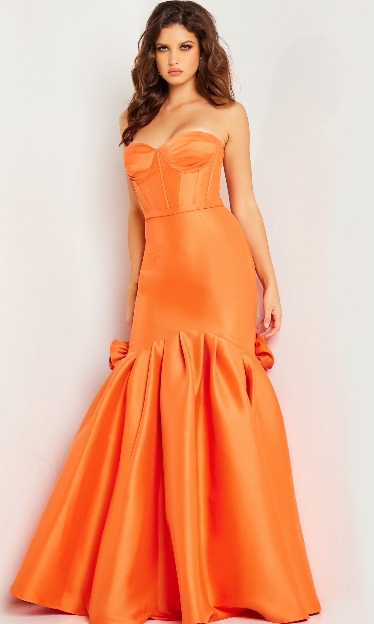 A woman stands against a white background wearing the Jovani Strapless Long Mermaid Prom Dress 24613, featuring a form-fitting orange satin bodice and a flared skirt.